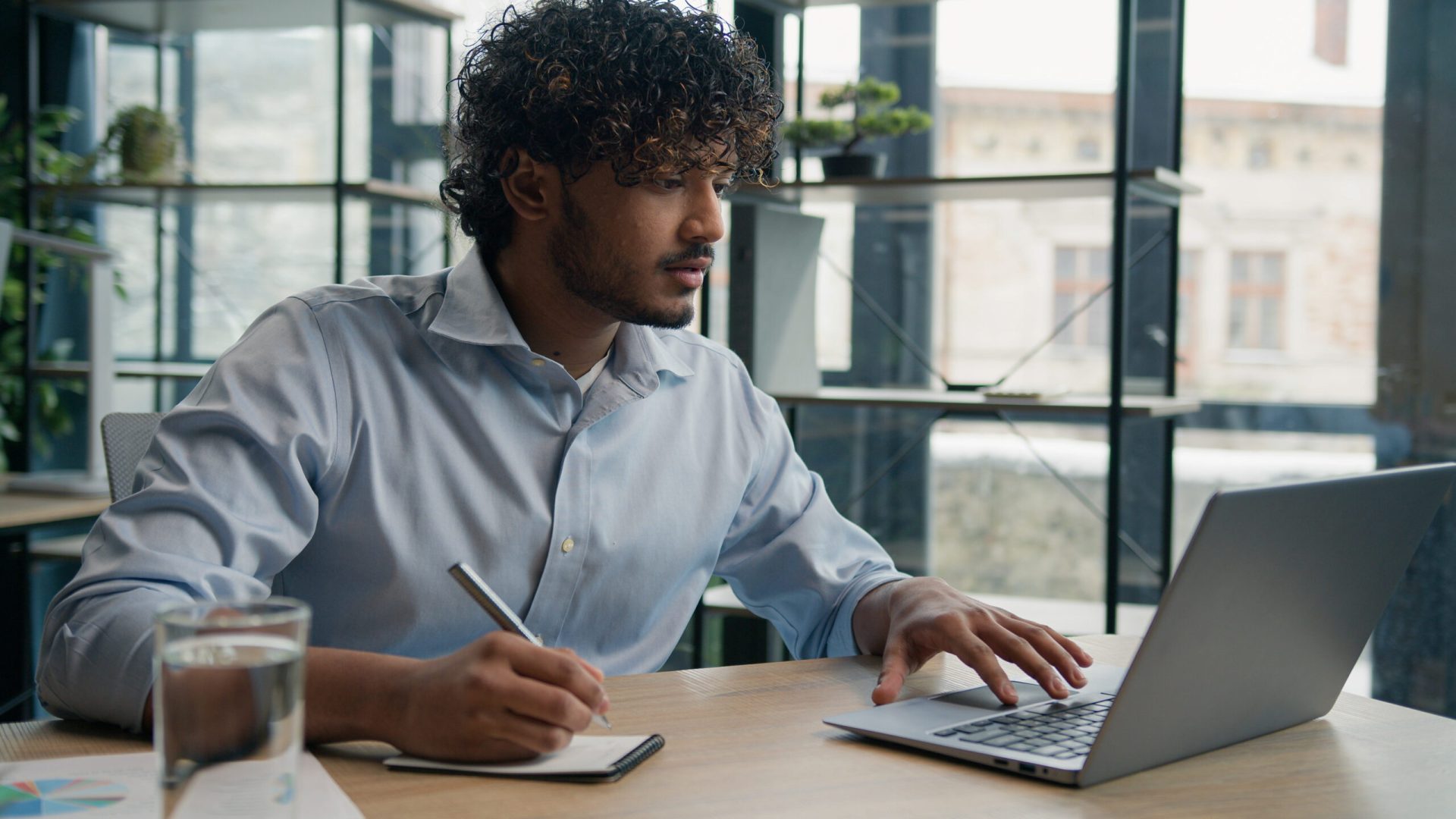 Indian Arabian man accountant writer business entrepreneur businessman write notes in notebook latino guy writing ideas report paperwork on office table studying online with laptop educational course. High quality 4k footage